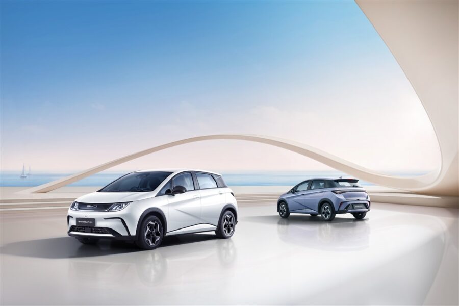 BYD Dolphin hai màu trắng và xám xanh trước công trình kiến trúc uốn cong bên bờ biển